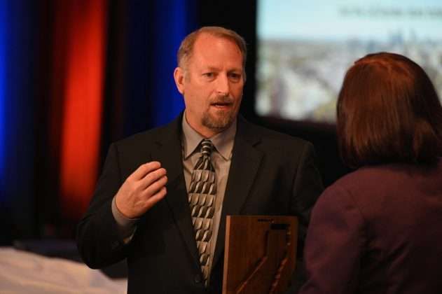 A man holding a framed plaque gestures during a conversation with a woman.