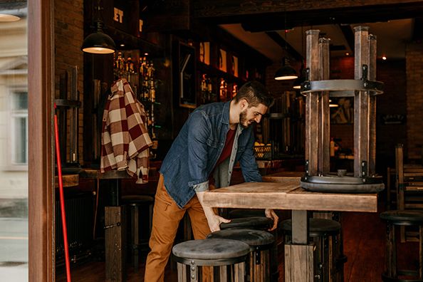 A worker wipes a restaurant table beside upside-down stools after service.