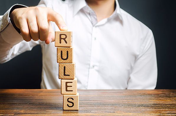 A person stacks wooden letter blocks vertically to spell RULES.