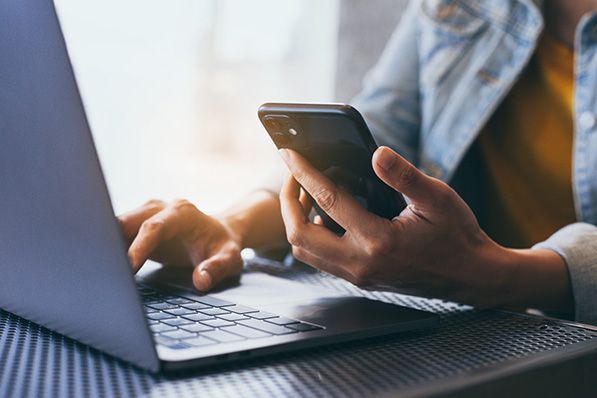 A person uses a smartphone while typing on a laptop.