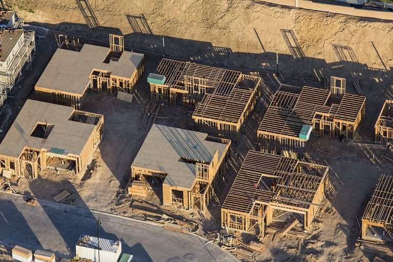 Aerial view of several houses under construction, showing wooden framing, foundations and bare ground.