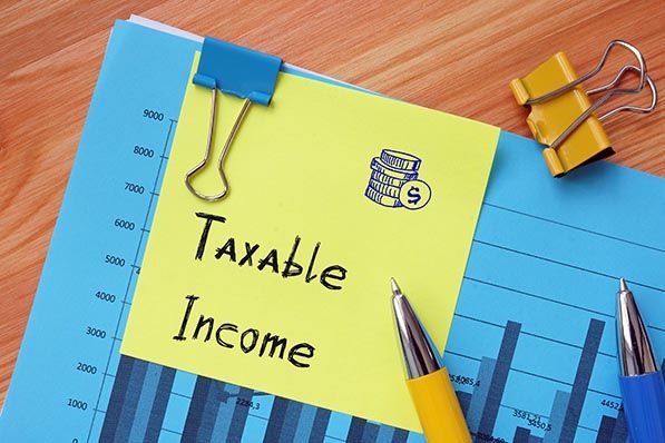 A yellow note reading Taxable Income rests on a blue chart beside pens and binder clips.