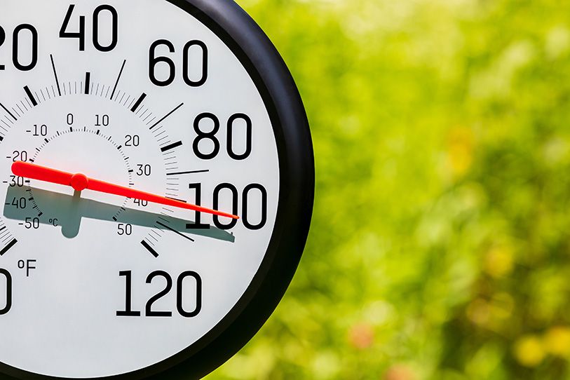 An outdoor dial thermometer reads around 100 degrees Fahrenheit against a green background.