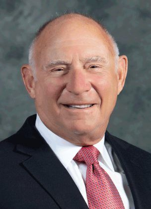 Portrait of a smiling bald man wearing a dark suit, white shirt and red tie.