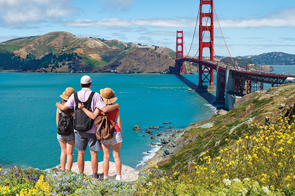 Three travelers with backpacks stand together overlooking the Golden Gate Bridge.