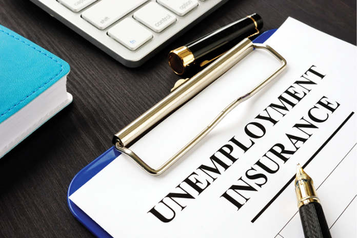 An Unemployment Insurance form on a clipboard beside a pen, notebook and keyboard.