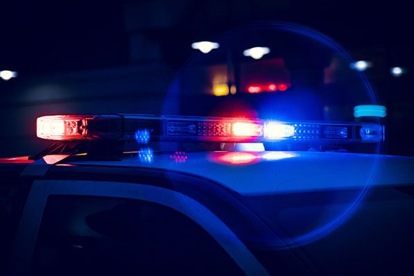 Red and blue emergency lights flash on the roof of a police car at night.
