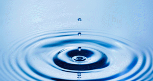 A falling water droplet creates concentric ripples on a blue surface.