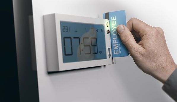A hand holds an employee card beside an electronic time clock displaying 07:59.