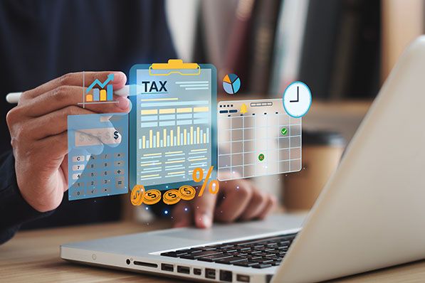 A person works at a laptop behind overlaid tax charts, a calculator and calendar graphics.