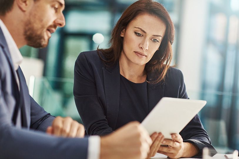 Two businesspeople review a tablet together at a desk.