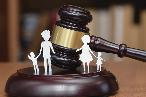A judge's gavel with white paper silhouettes of adults and children on its sound block.