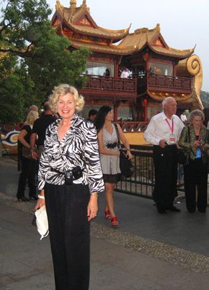A woman poses outdoors before an ornate building with curved golden roofs.