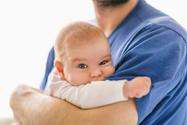 An adult in a blue shirt cradles a baby against their chest.