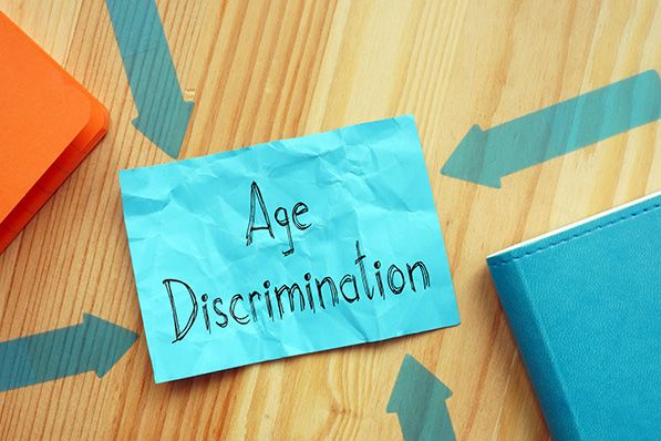 A blue note reading Age Discrimination lies on a desk surrounded by inward-pointing arrows.
