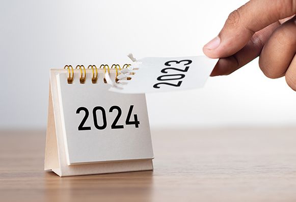 A hand turns a desktop calendar page from 2023 to 2024.