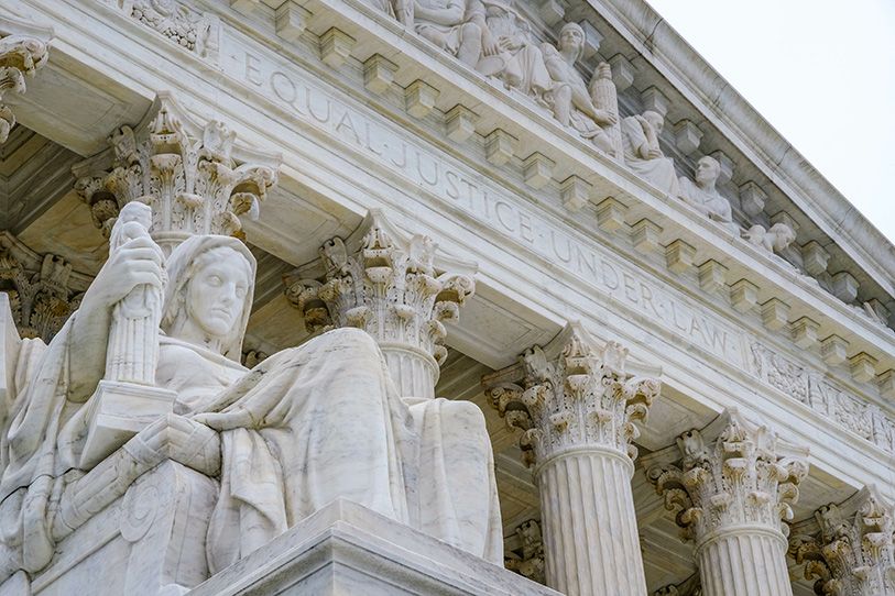 Close-up of the U.S. Supreme Court facade, columns and a seated marble statue.