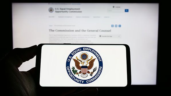 A phone displays the Equal Employment Opportunity Commission seal in front of an EEOC webpage.