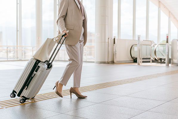 A person in business attire pulls a silver rolling suitcase through a bright, modern transport hub.