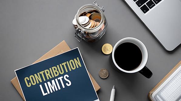 A Contribution Limits booklet beside a jar of coins, coffee cup and laptop.