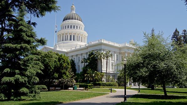 California State Capitol seen across a lawn and footpath among trees.