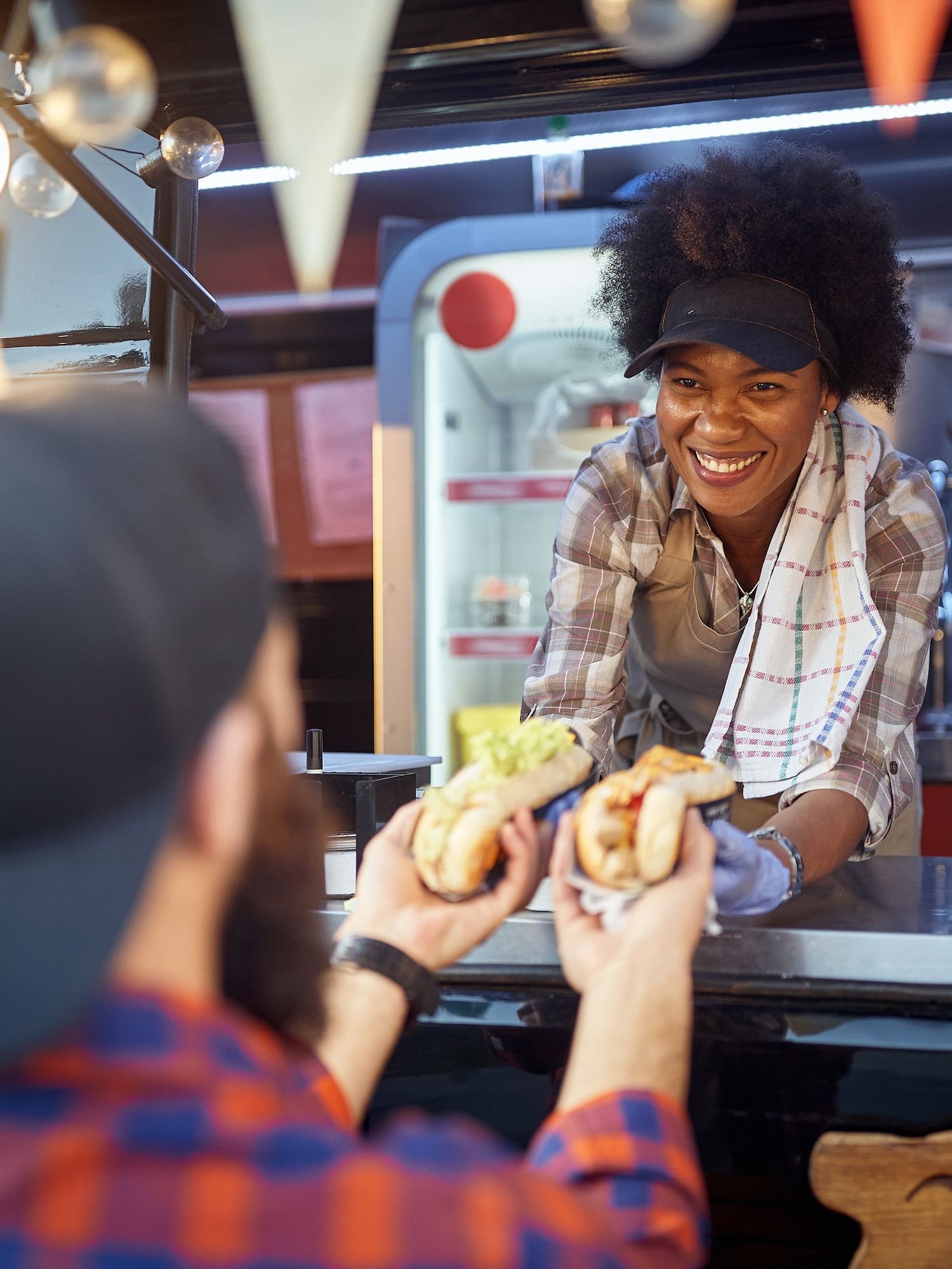 A smiling food truck worker hands food to a customer through a service window.