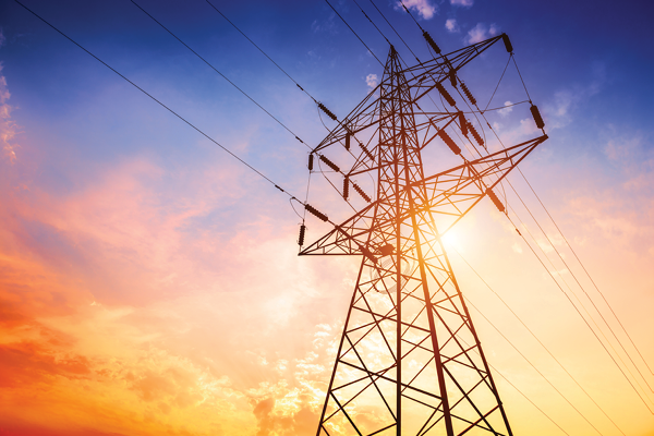 An electricity transmission tower and power lines against a colorful sunset.