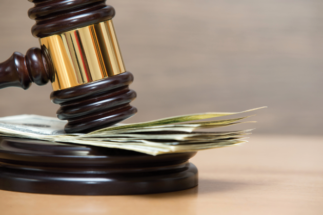 A judge's gavel rests on a stack of banknotes atop a wooden sound block.