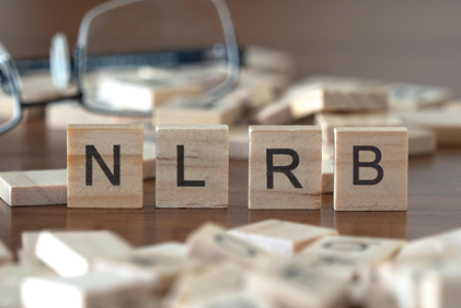 Wooden letter blocks spell NLRB beside eyeglasses and scattered tiles.