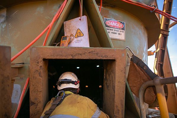 A worker wearing a helmet enters an industrial opening beneath danger warning signs.