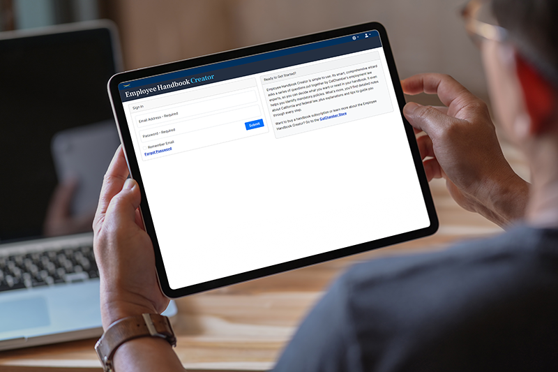 A person holds a tablet displaying an Employee Handbook Creator webpage.