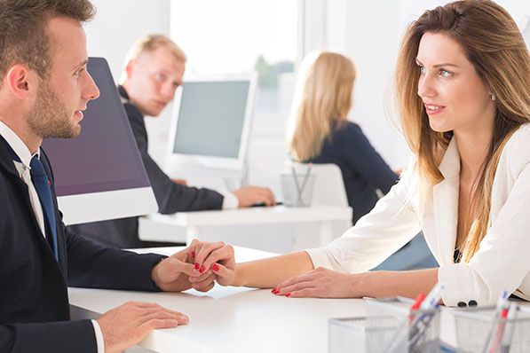 Two office workers face each other across a desk while holding hands.