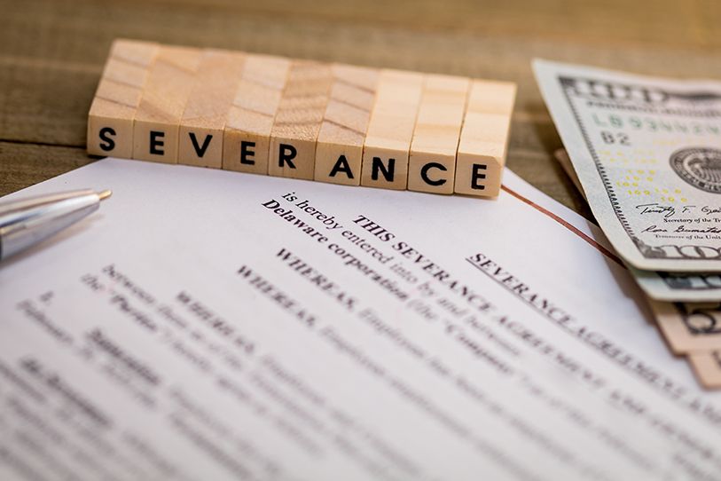 Wooden tiles spell SEVERANCE above paperwork beside U.S. banknotes.