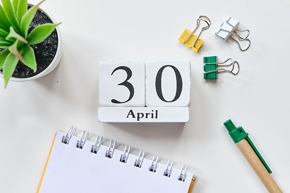 An April 30 desk calendar beside a notebook, pens, binder clips and a small plant.