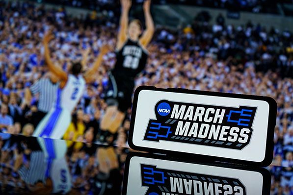 A smartphone displays the NCAA March Madness logo in front of a basketball game.