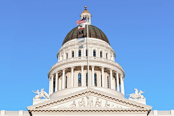 The white dome and sculpted pediment of the California State Capitol against a clear blue sky.