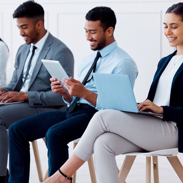 Three seated people in business attire use a tablet, laptop and paperwork.