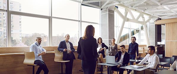 A presenter leads a discussion with coworkers seated in a bright meeting area.