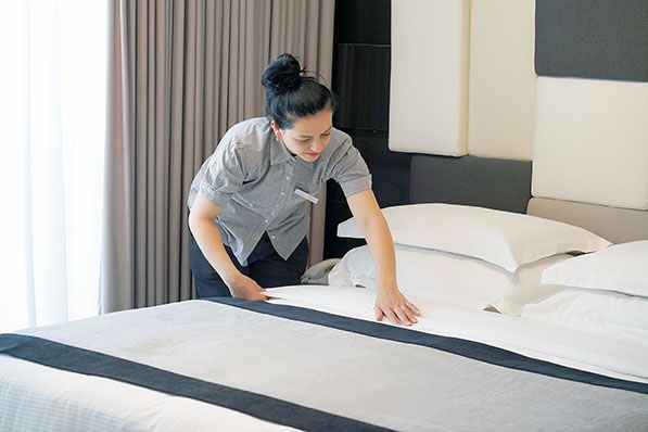 A housekeeper making a bed in a hotel room.