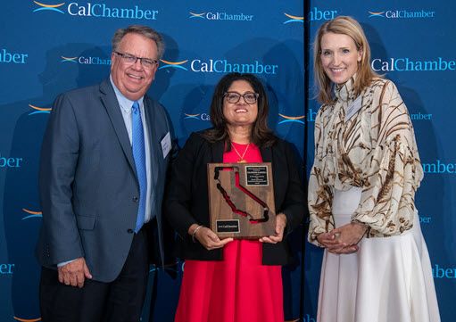 A woman holding an award plaque stands between a man and another woman before a CalChamber backdrop.