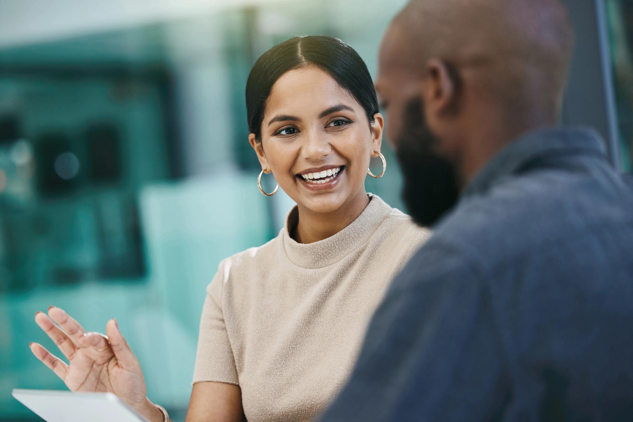 Smiling woman in a beige top gesturing while talking to a man seen from the back.