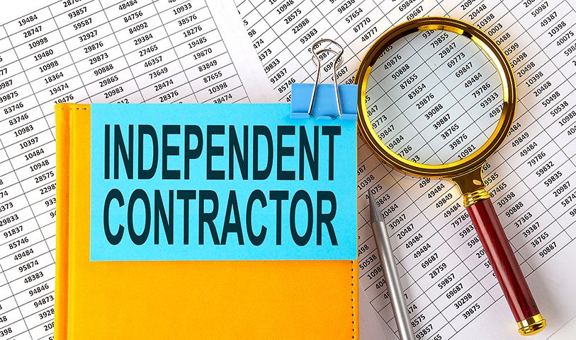 A card labeled INDEPENDENT CONTRACTOR lies on a folder beside a magnifying glass and printed tables.