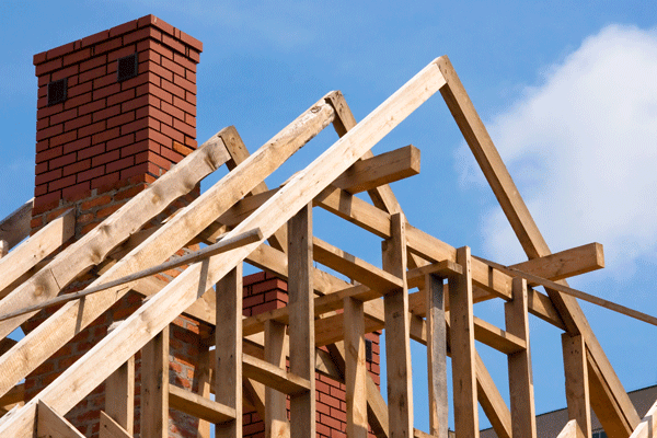 Wooden roof framing surrounds a red brick chimney beneath a blue sky.