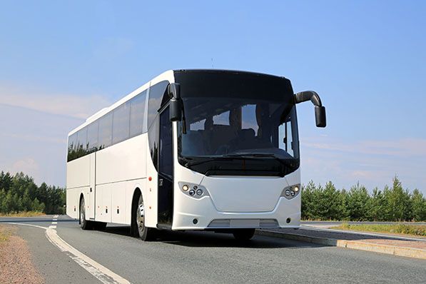 A white tour bus drives on a road under a blue sky.