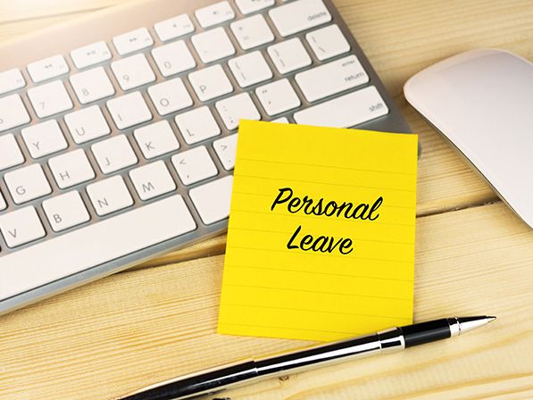 Yellow note reading Personal Leave beside a keyboard, mouse and pen.