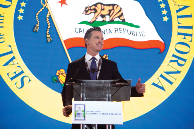 A man speaks at a clear lectern in front of a large California state seal.