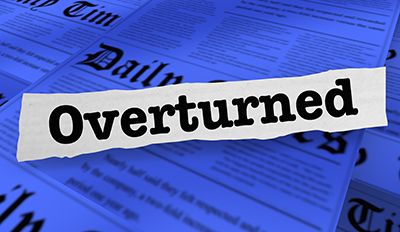 A paper strip reading Overturned lies across blue-tinted newspapers.