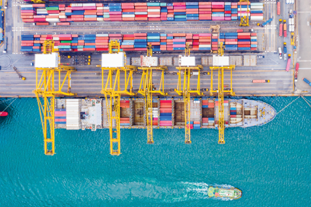Aerial view of a container ship at a port with yellow cranes and rows of colorful containers.