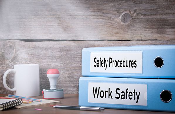 Blue binders labeled Safety Procedures and Work Safety sit on an office desk.