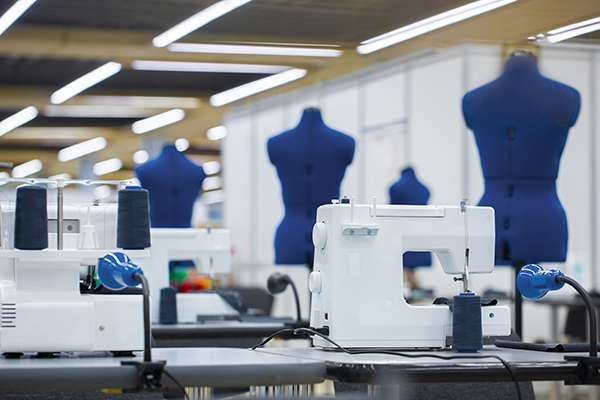 Rows of sewing machines and blue dress forms in a garment manufacturing workshop.
